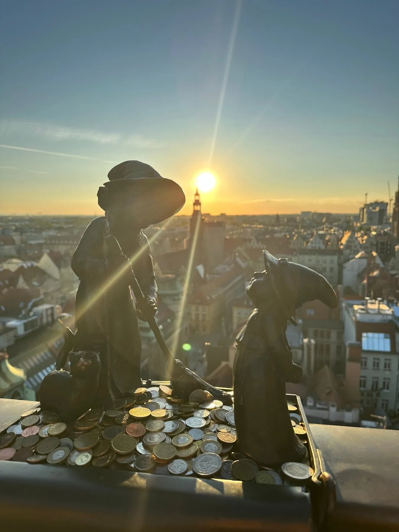 Bronze statues and coins overlooking Gdańsk at sunset